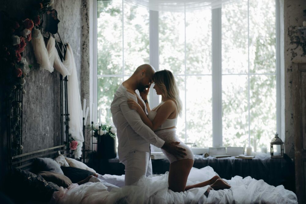 A couple shares an intimate moment in a chic, sunlit bedroom with vintage decor.